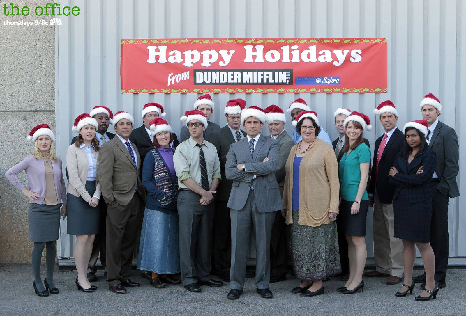 戴著聖誕帽的辦公室員工在 Dunder Mifflin 標誌前為節日照片擺姿勢。