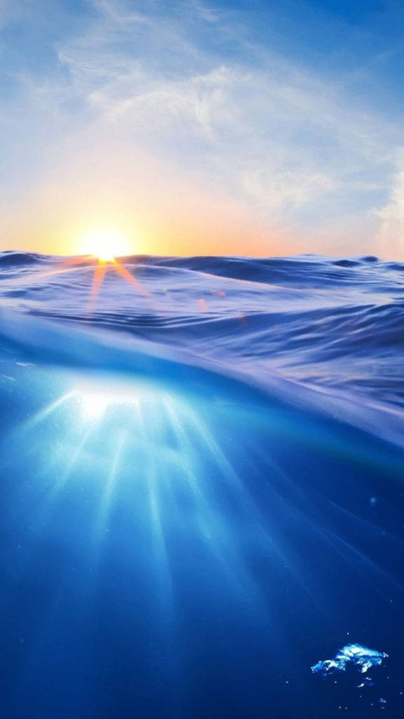 近拍海浪日出自然風景 壁紙 — 海洋上的日落，金色光線穿過波浪，照亮藍色水下光線。