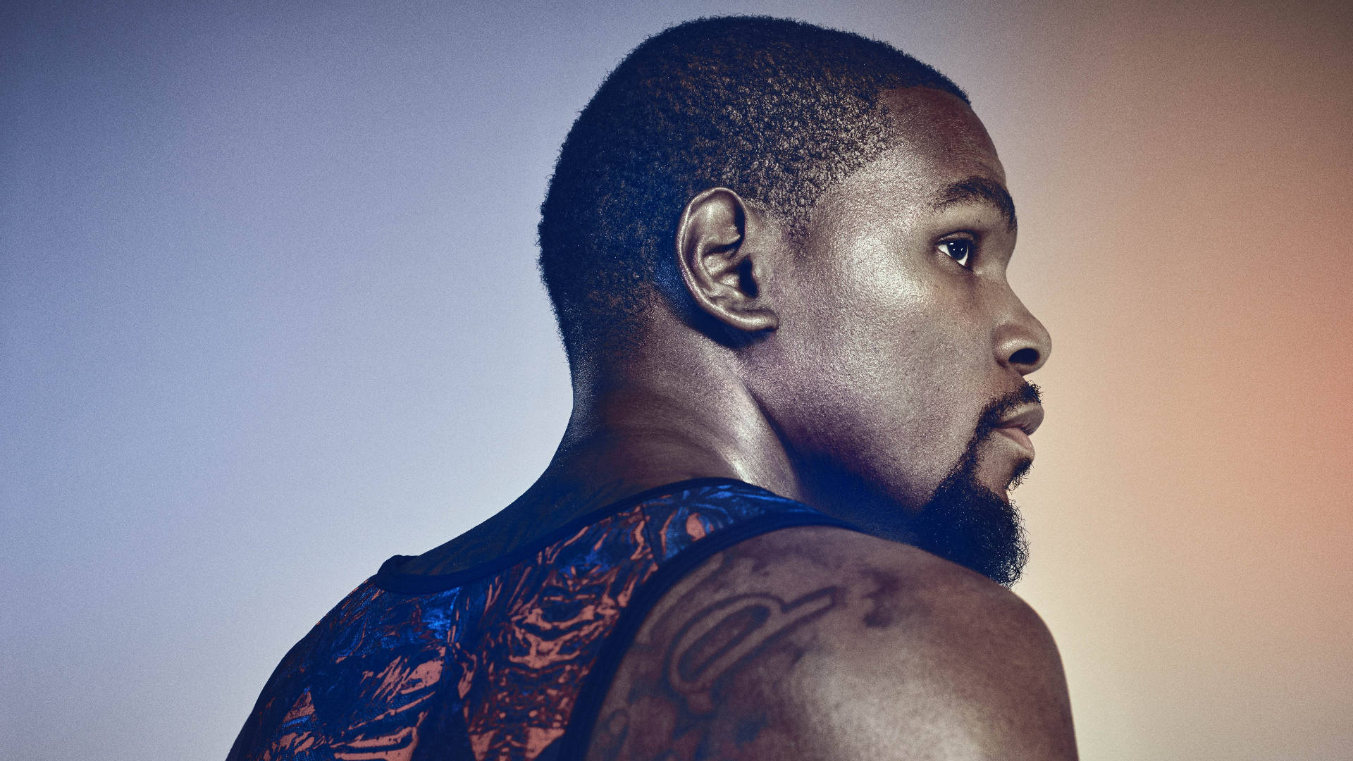 一個留鬍子、肩膀有紋身的男人在藍橙漸變背景的攝影棚肖像。