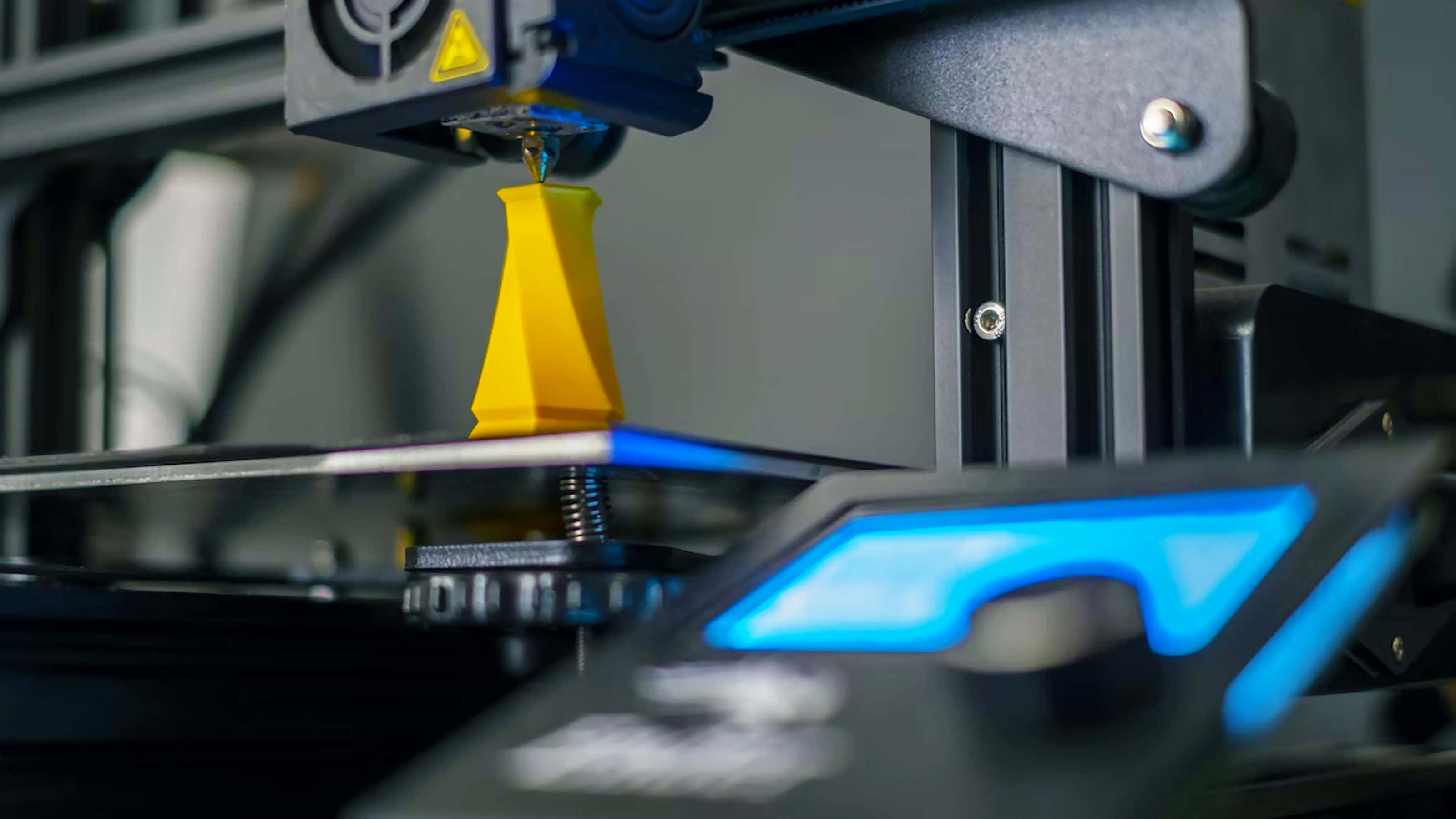 3d Printer 桌布 壁紙 — 近距離拍攝3D打印機在帶有藍色LED照明的打印床上擠出亮黃色線材以構建幾何物體。