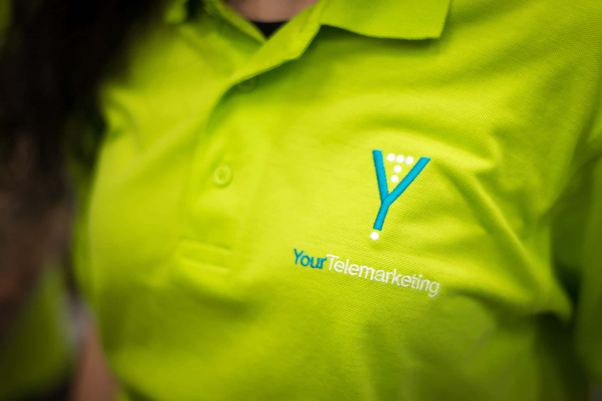 Telemarketing 桌布 壁紙 — 近距離拍攝一件鮮亮青檸綠色Polo衫，胸前繡有藍色「Y」標誌及「YourTelemarketing」文字。
