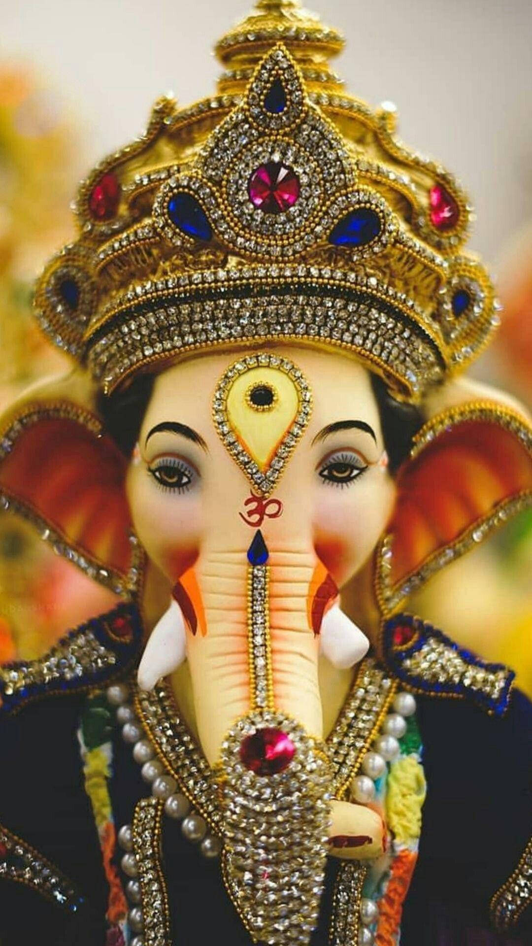 ganesh iPhone 桌布 壁紙 — 近距離拍攝一位裝飾華麗的印度教象頭神Ganesha，戴著金色皇冠、寶石和精緻珠寶。