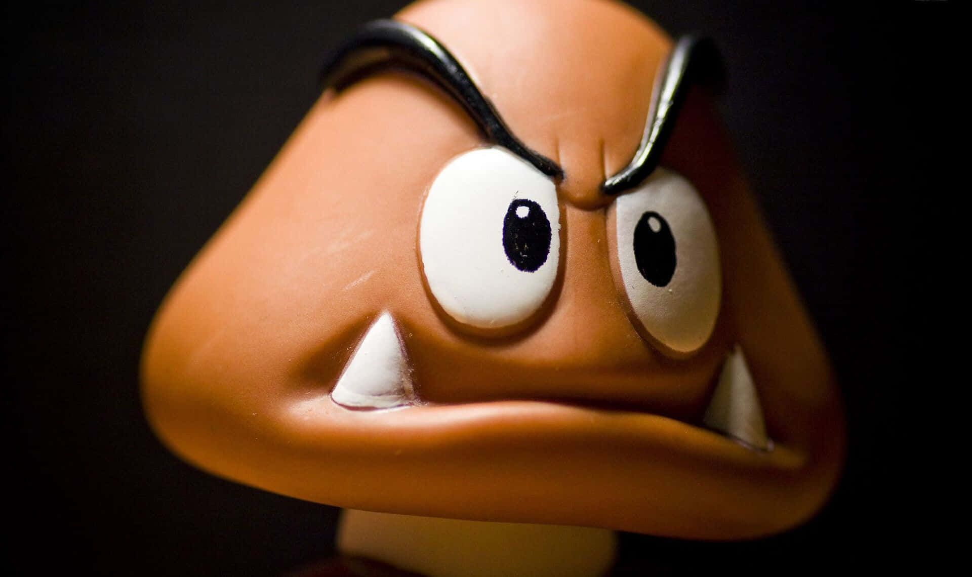 Goomba 桌布 壁紙 — 近距離拍攝一個帶有尖銳眉毛和尖牙的橙色威脅性Goomba玩具，背景為深色。