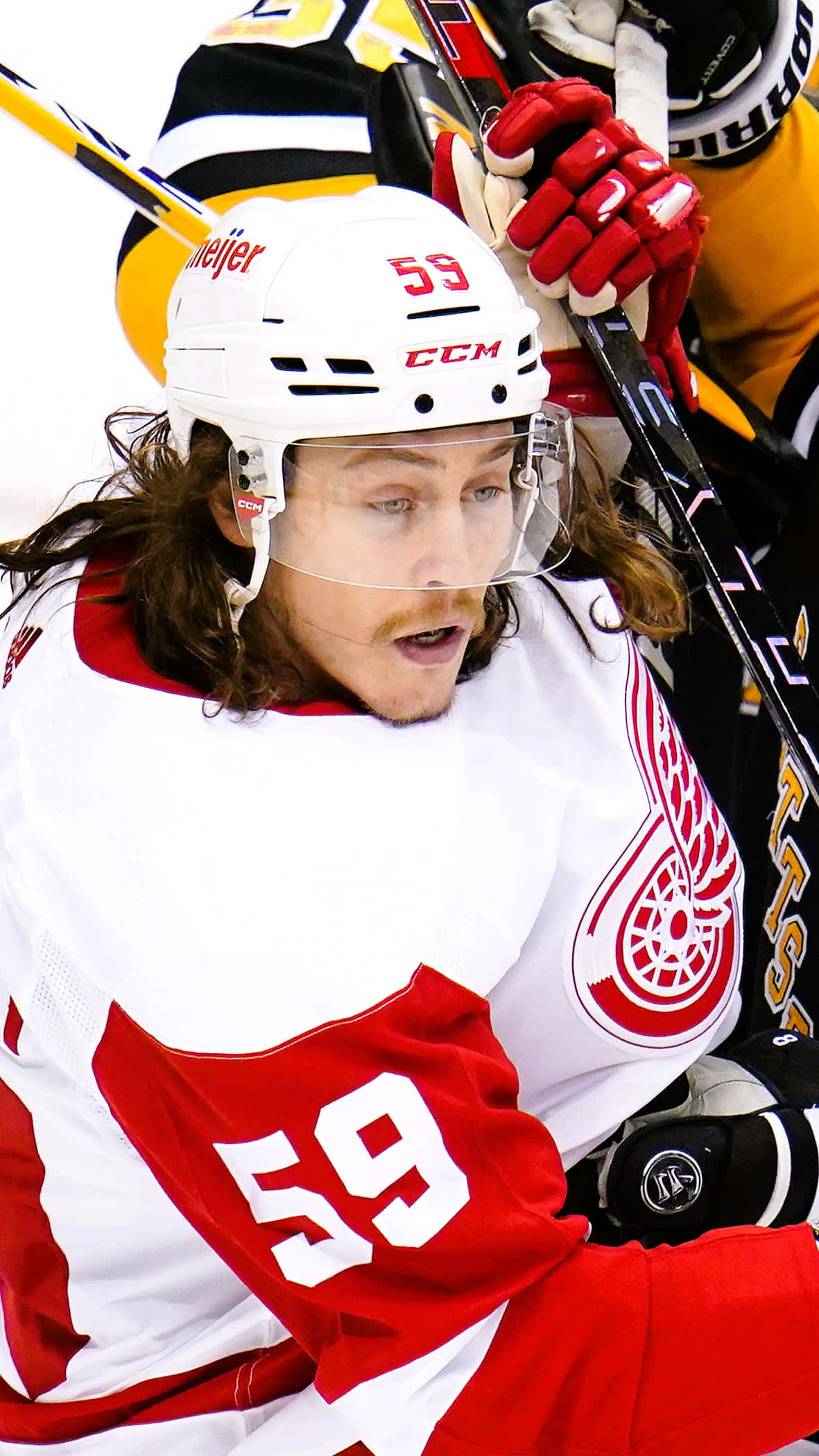 Tyler Bertuzzi 桌布 壁紙 — 近距離拍攝一名身穿紅白色底特律紅翼隊59號球衣、長髮且神情專注的冰球運動員。