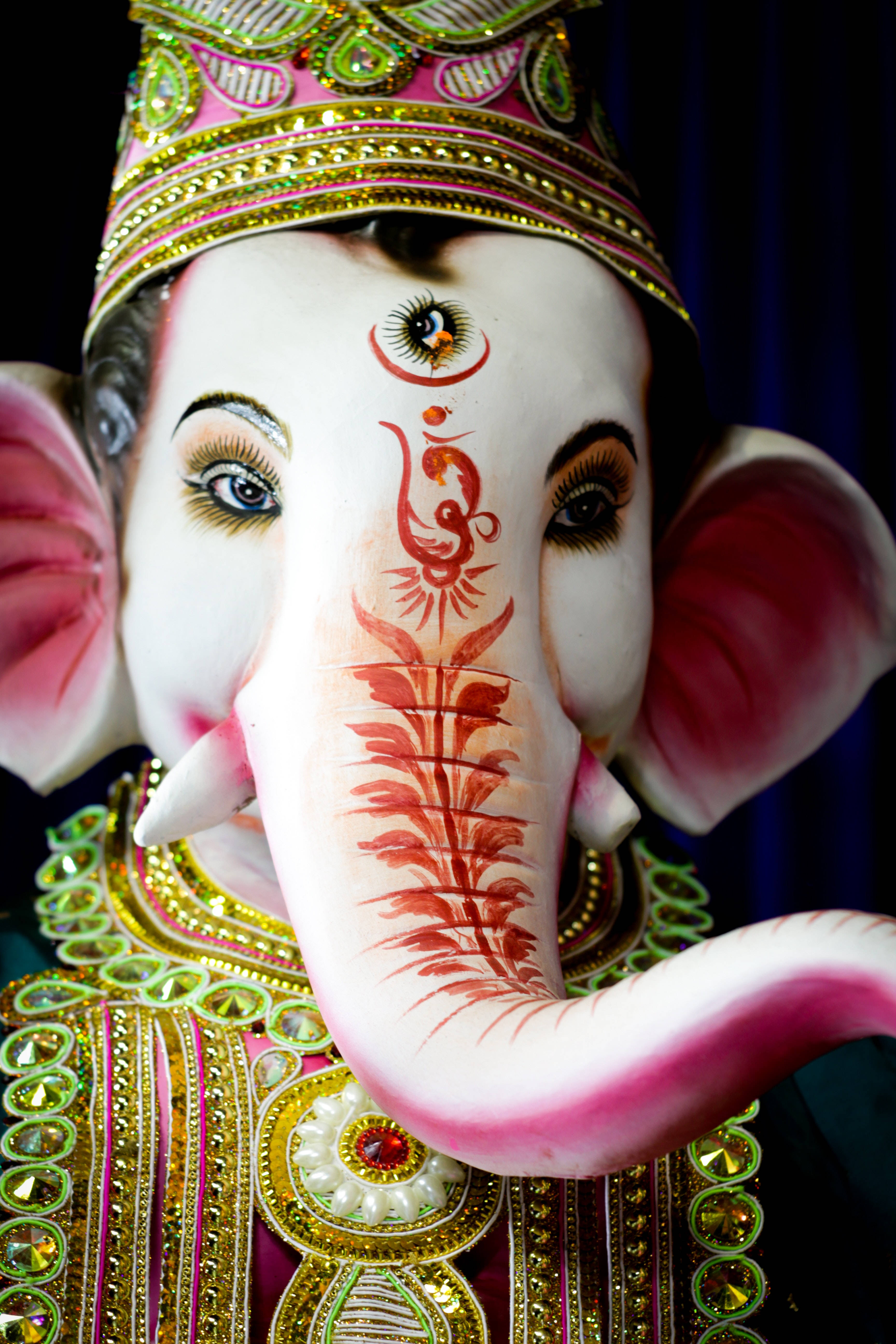Ganesh 桌布 壁紙 — 近距離拍攝一尊裝飾鮮豔的象頭神像，有粉紅色耳朵、金色皇冠和紅色指甲花圖案在象鼻上。