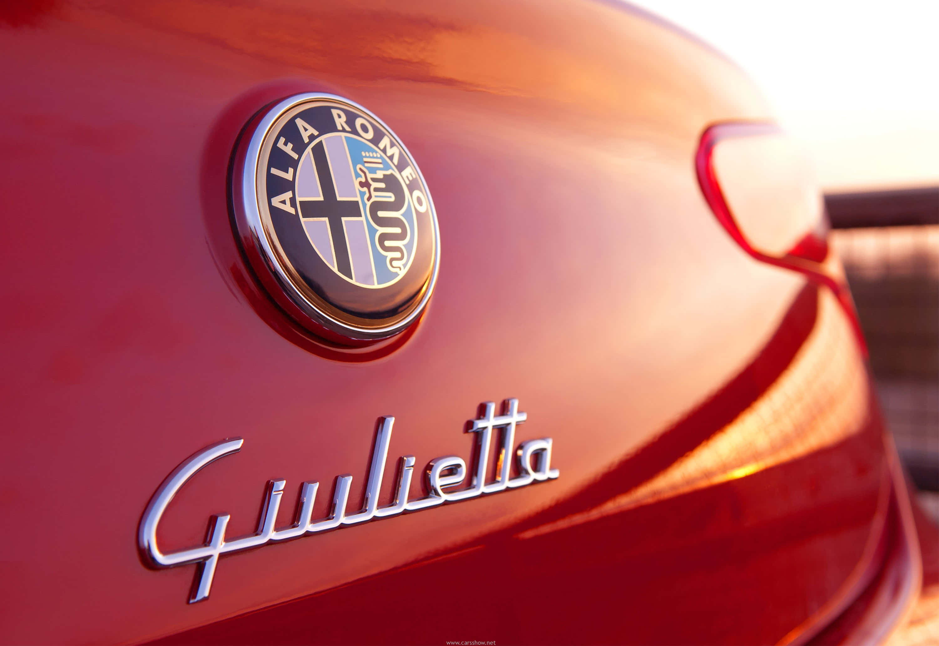 Alfa Romeo Giulietta 桌布 壁紙 — 近距離拍攝光澤紅色 Alfa Romeo Giulietta 標誌，捕捉金色夕陽光芒。