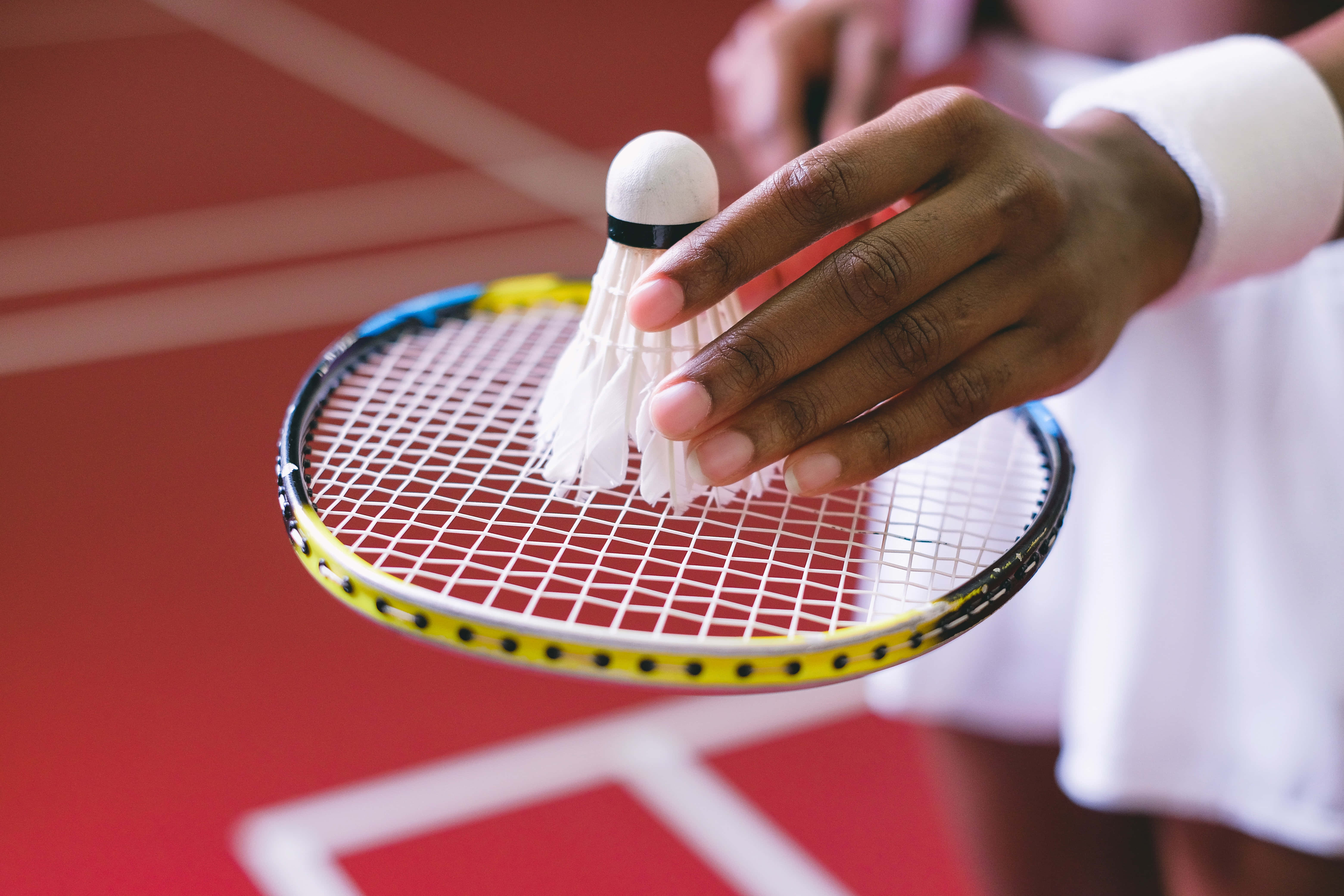 Badminton 桌布 壁紙 — 近距離拍攝球員手持羽毛球拍，羽毛球在紅色場地上方。