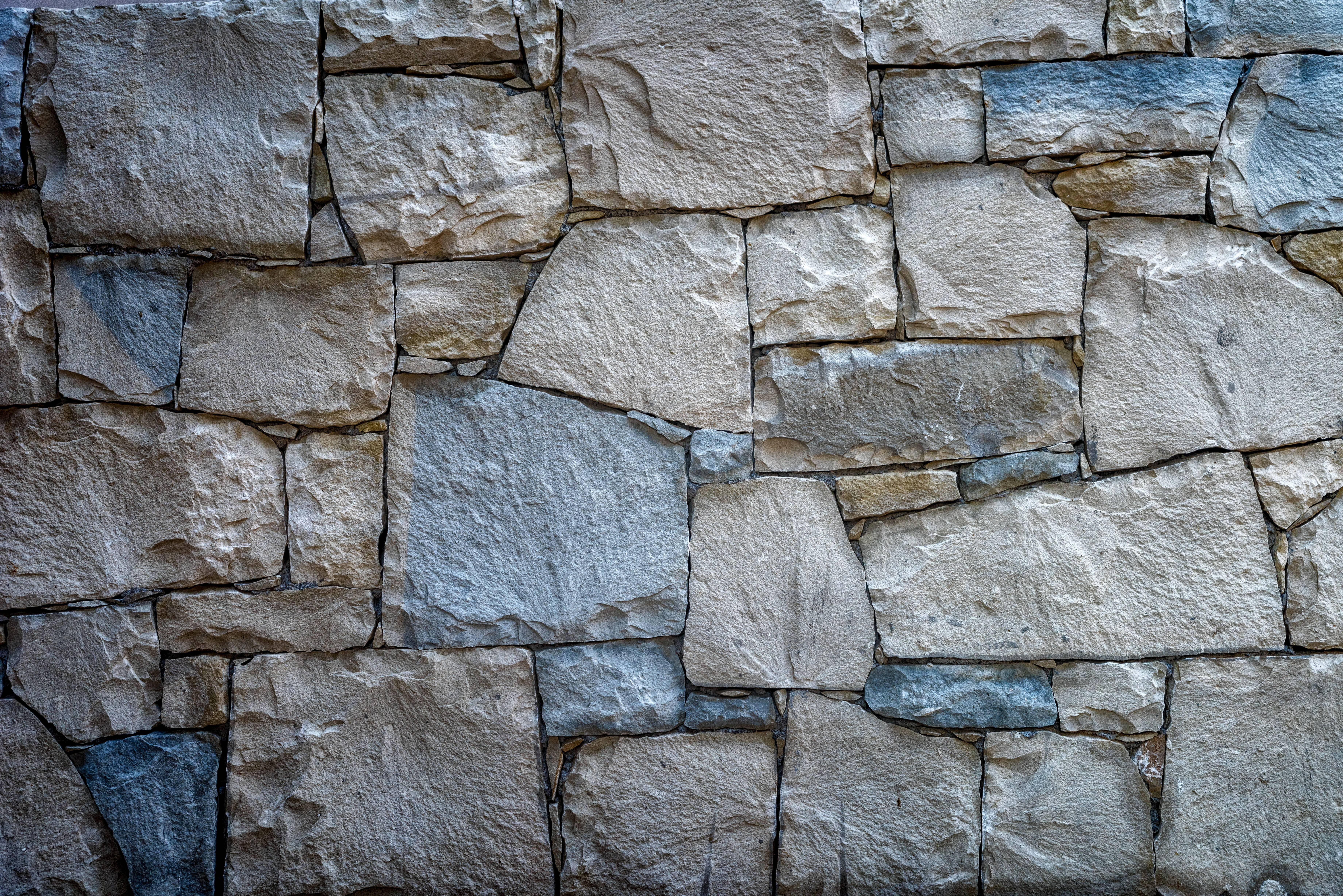 Stone Wall 桌布 壁紙 — 近距離拍攝的堅固天然石牆，具有多種米色、灰色和棕褐色調，以及粗糙的紋理表面。