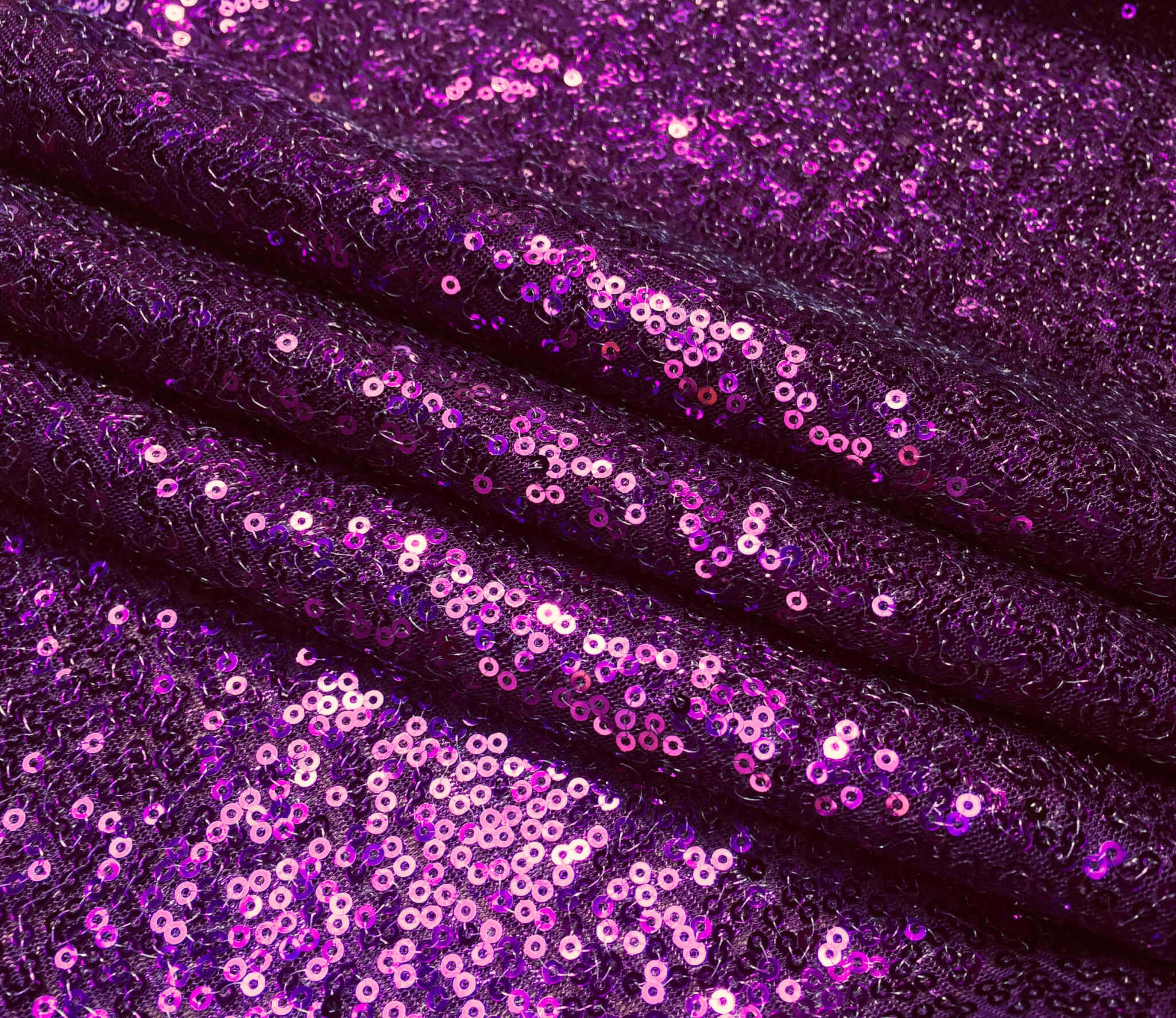 Purple Sequins 桌布 壁紙 — 近距離拍攝的濃郁紫色布料，上面密密麻麻覆蓋著閃閃發光的粉紅色亮片，營造出奢華的紋理表面。