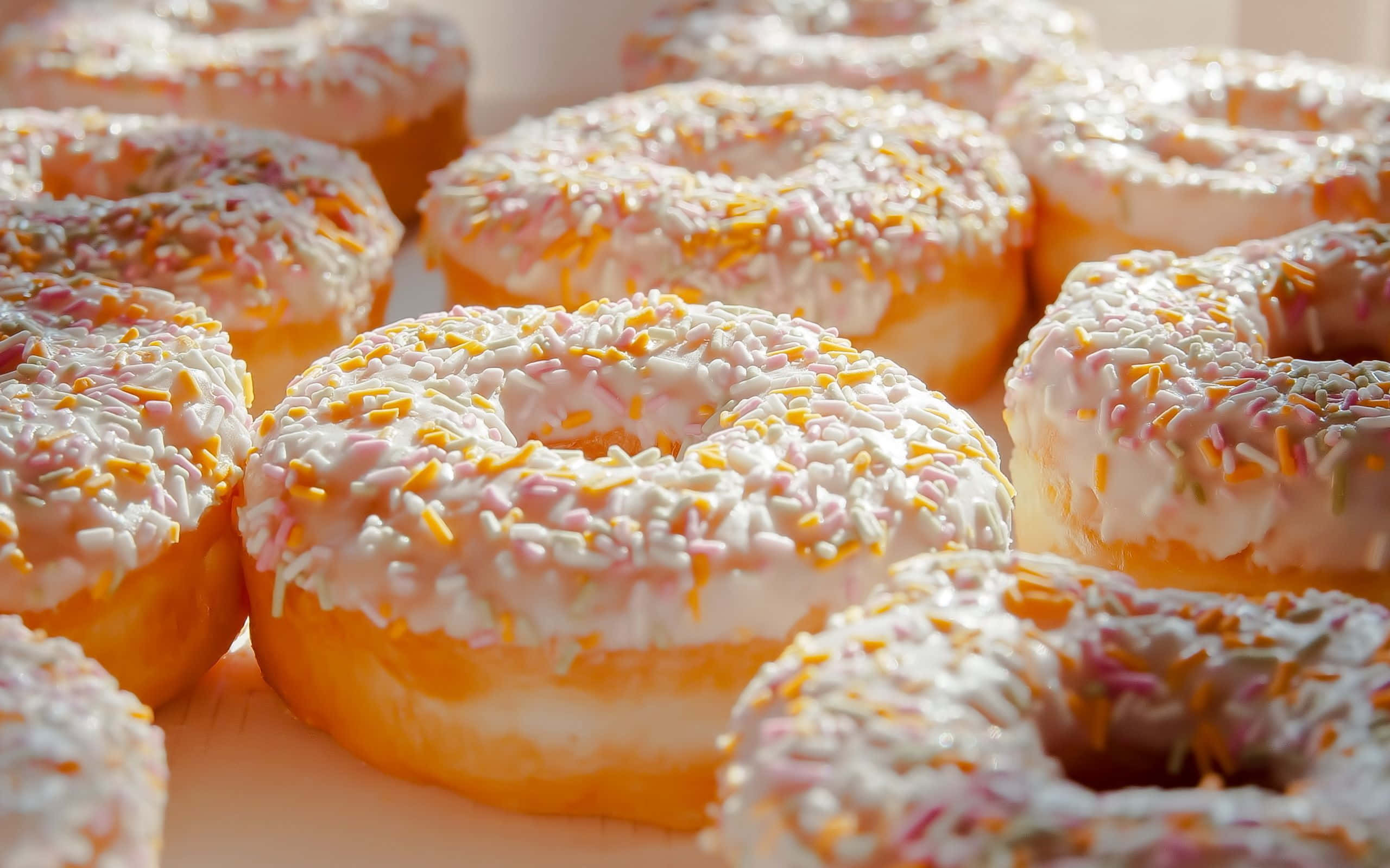 donuts 桌布 壁紙 — 近距離拍攝的糖霜冬甩，上面灑滿彩色糖粒，沐浴在溫暖的金色光芒中。