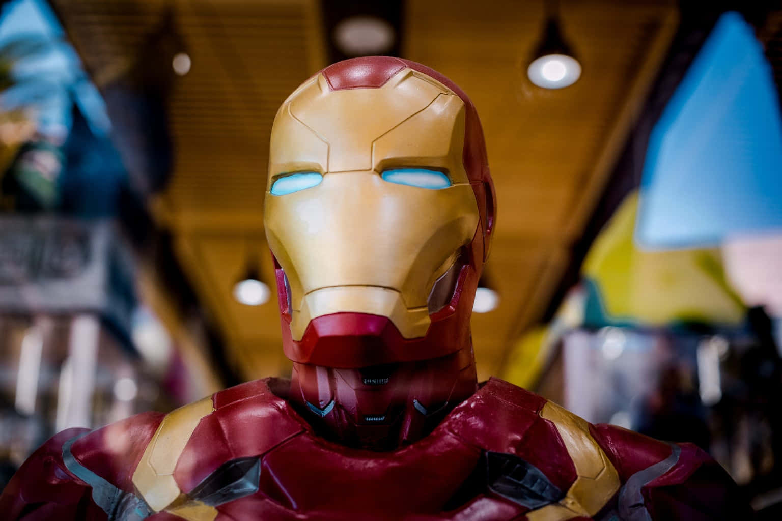 Superhero Movies 桌布 壁紙 — 近距離拍攝的詳細鐵甲奇俠套裝，帶有發光的藍色眼睛和紅金色盔甲，處於昏暗的室內環境中。