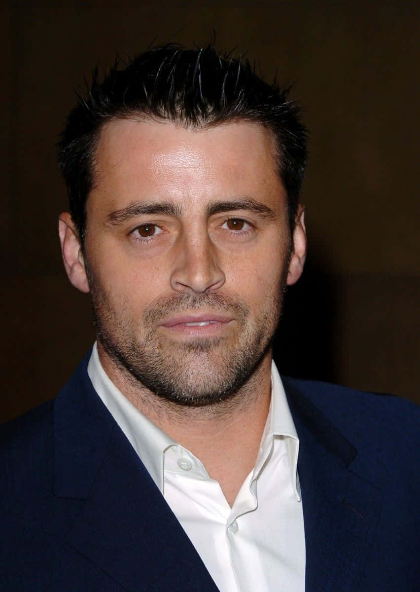 Matt Leblanc 桌布 壁紙 — 近距離肖像，一名深色刺蝟頭、留鬚根的男子，身穿海軍藍西裝及白恤衫，背景深色。