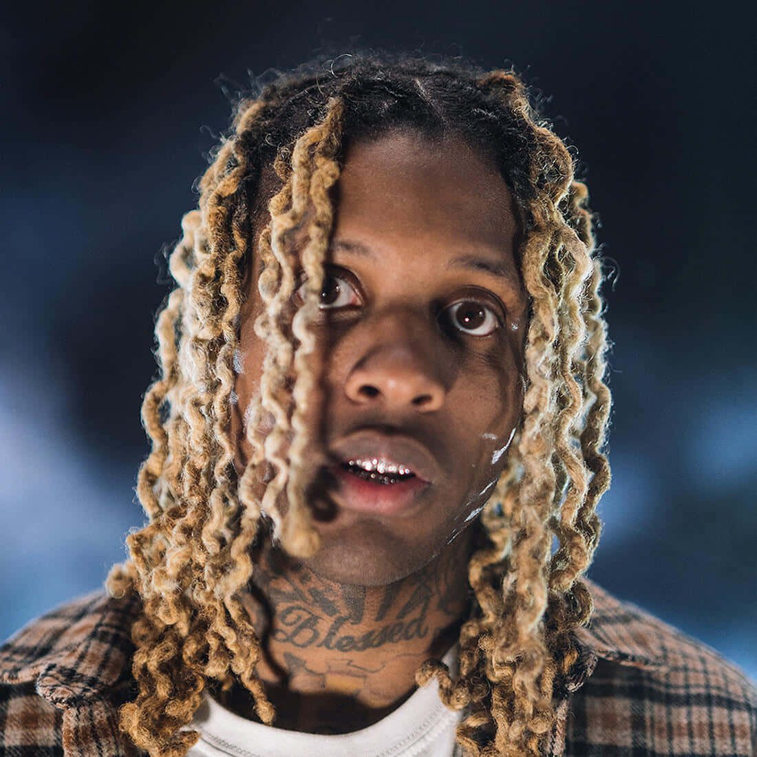 lil durk 桌布 壁紙 — 近距離肖像，一名男子留著長長的金色辮子，頸部有紋身，背景是模糊的藍色。