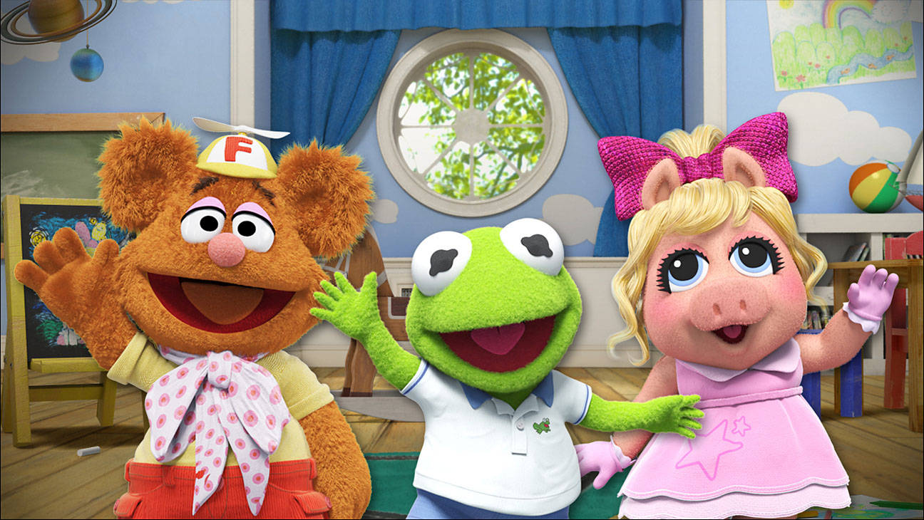 迪士尼《布偶娃娃》可愛角色 壁紙 — Fozzie、Kermit 同 Miss Piggy 喺一個有藍色牆壁同圓窗嘅色彩繽紛 Muppet 遊戲室入面開心咁揮手。