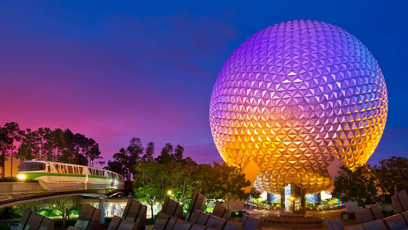 迪士尼EPCOT太空船地球主題公園縮放背景 壁紙 — 一個發光的紫色和金色測地線球體主導了黃昏場景，單軌列車在充滿活力的粉紅色和藍色天空下滑過。