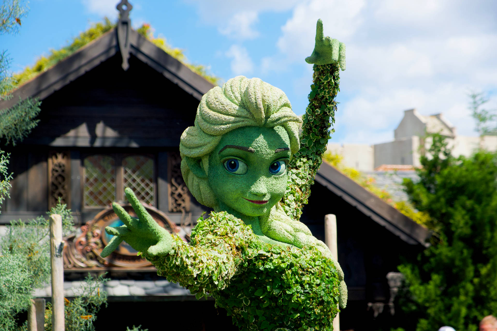 《冰雪奇緣》中艾莎的綠色修剪植物雕塑在木建築前揮手。