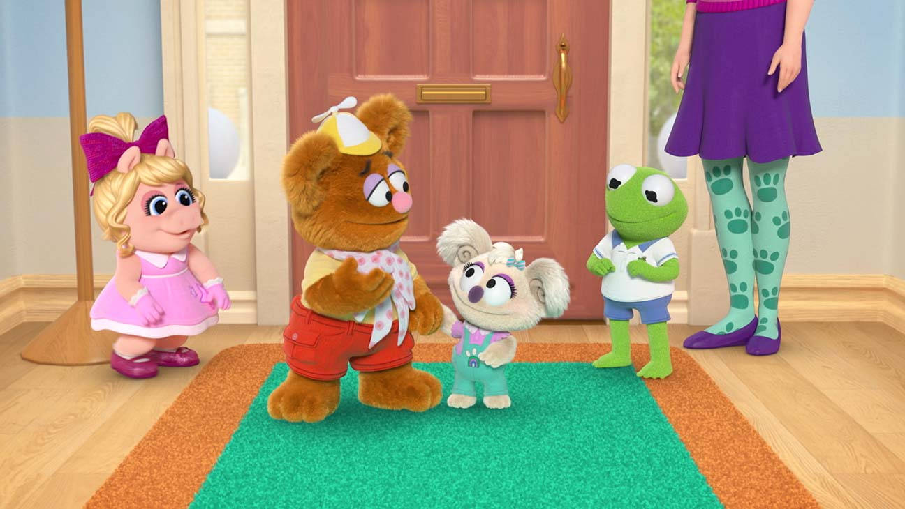 迪士尼小木偶寶寶 芝士熊與妹妹 壁紙 — Fozzie Bear、Kermit the Frog 和 Miss Piggy 與孩子們站在木門附近光線明亮的走廊裡。
