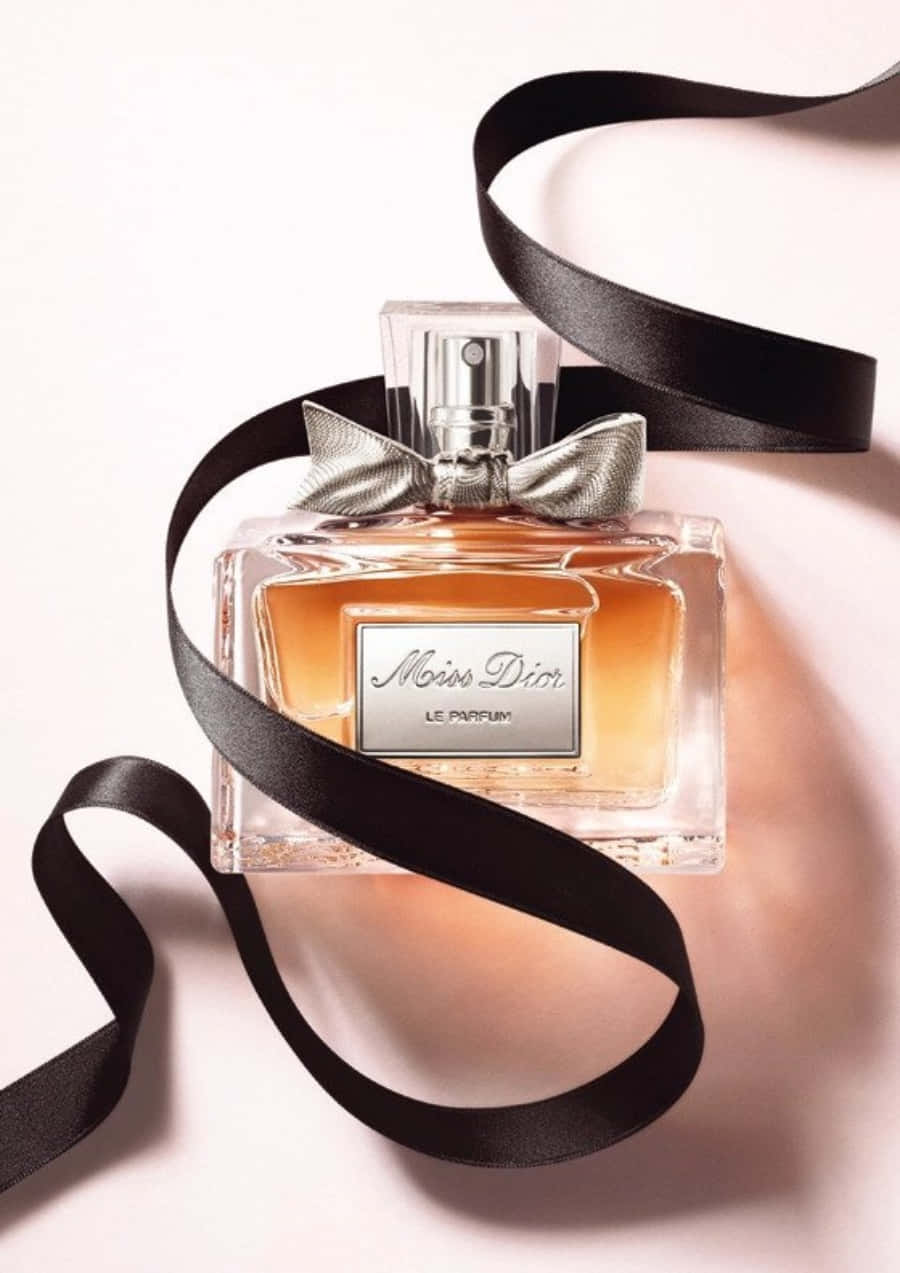 迪奧的奢華時尚殿堂 壁紙 — 一個時尚的 Miss Dior 香水瓶，裝有琥珀色液體和銀色蝴蝶結，放置在柔軟的粉紅色表面上，包裹著流動的黑色絲帶。
