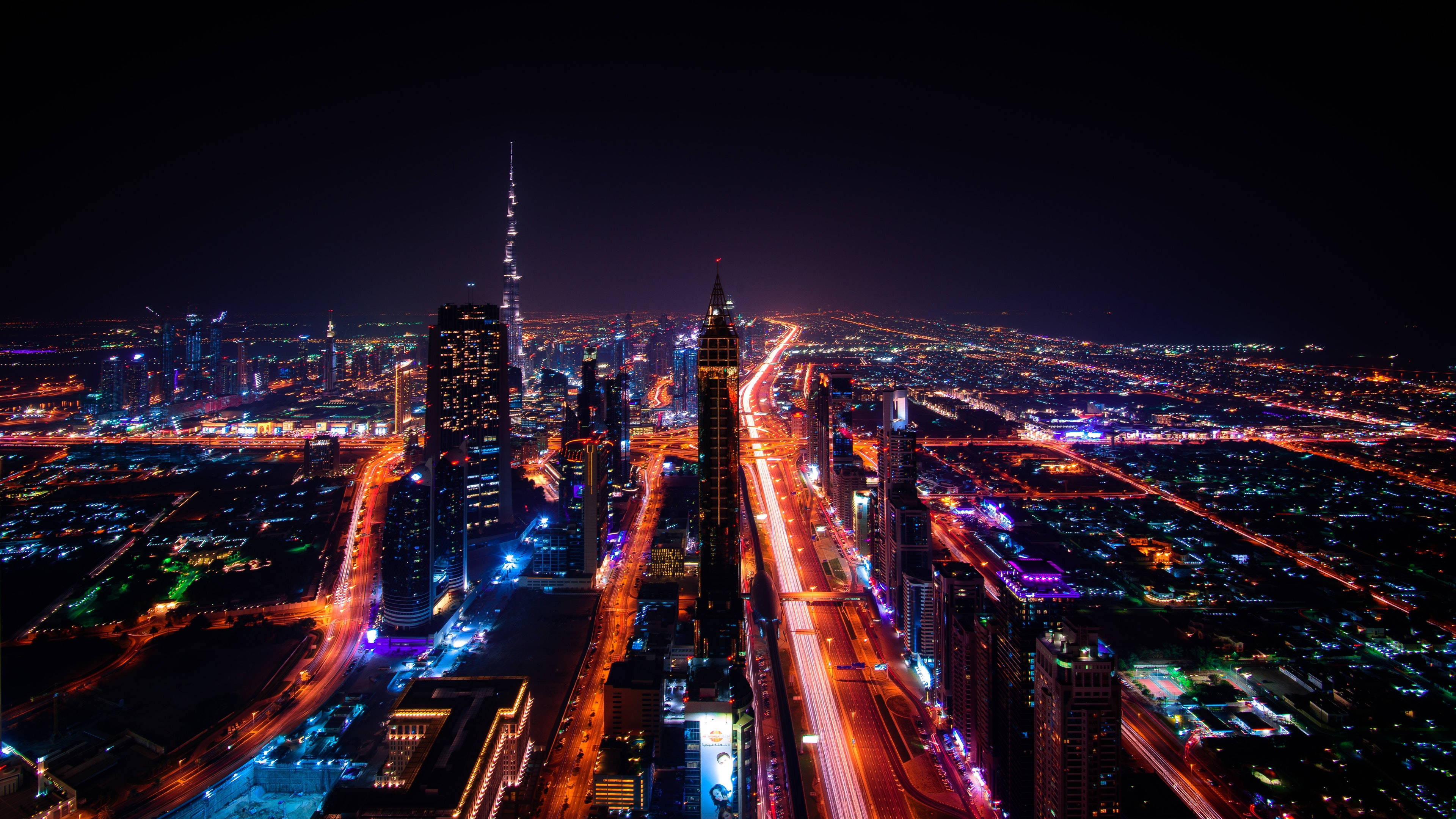 迪拜城市夜景 4K 壁紙 — 杜拜天際線的夜間空中景觀，哈利法塔在霓虹燈照亮的道路和摩天大樓中閃耀。