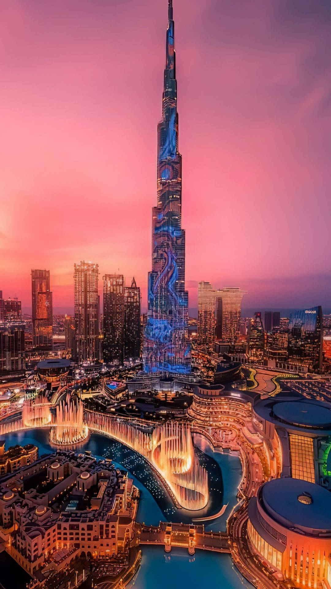 迪拜奇觀建築 壁紙 — 哈利法塔在日落時分聳立於杜拜天際線之上，天空呈現鮮豔粉紅色，下方噴泉燈光璀璨。
