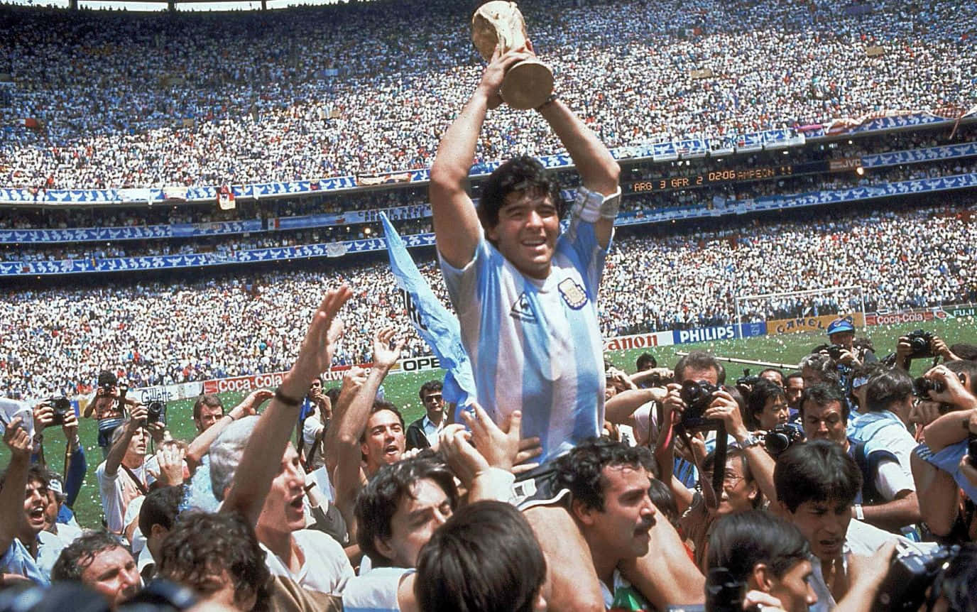 Diego Maradona 在球場上被歡呼的球迷包圍，手持世界盃獎盃。