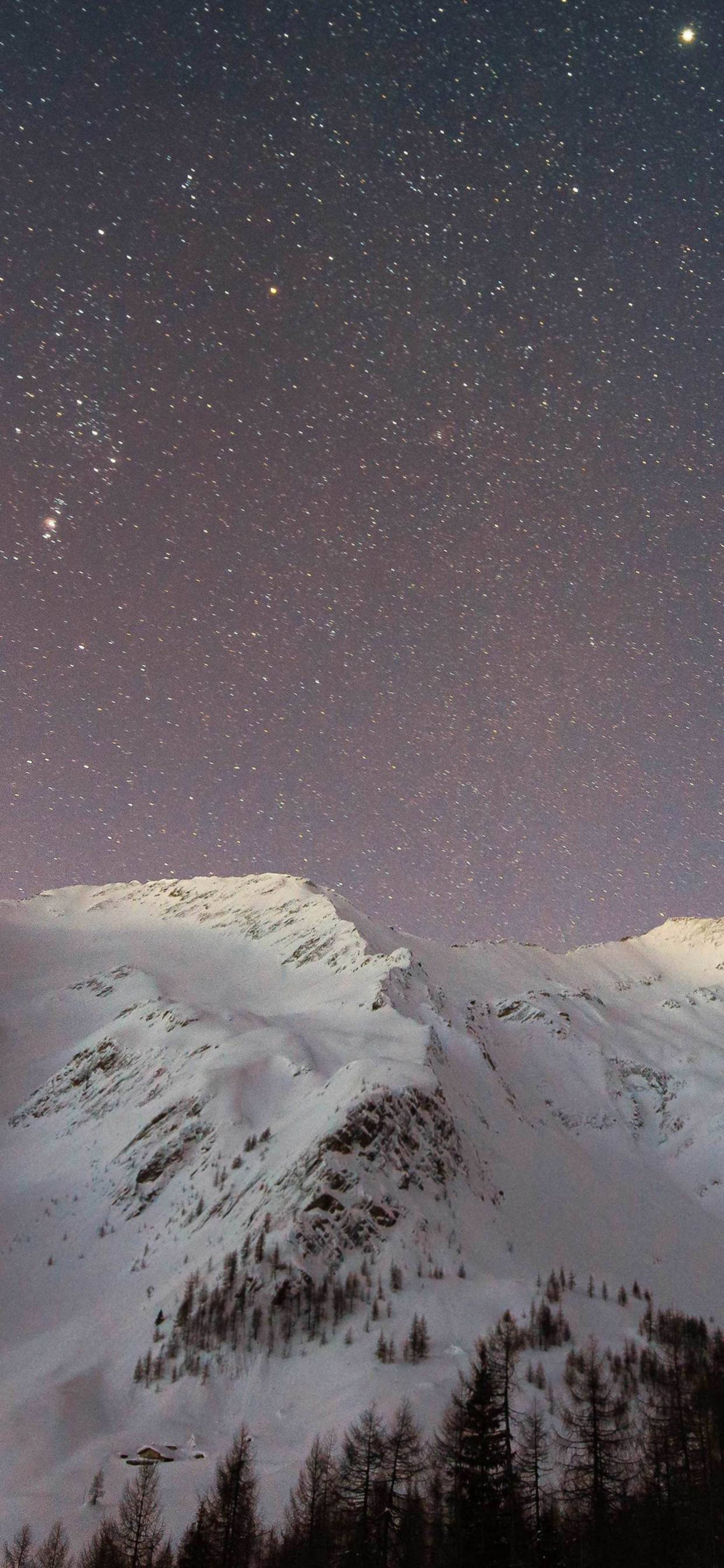 迷人 iPhone 13 Pro Max 配雪峰背景 壁紙 — 積雪的山峰在繁星點點的夜空下升起，夜空閃爍著紫色的極光。