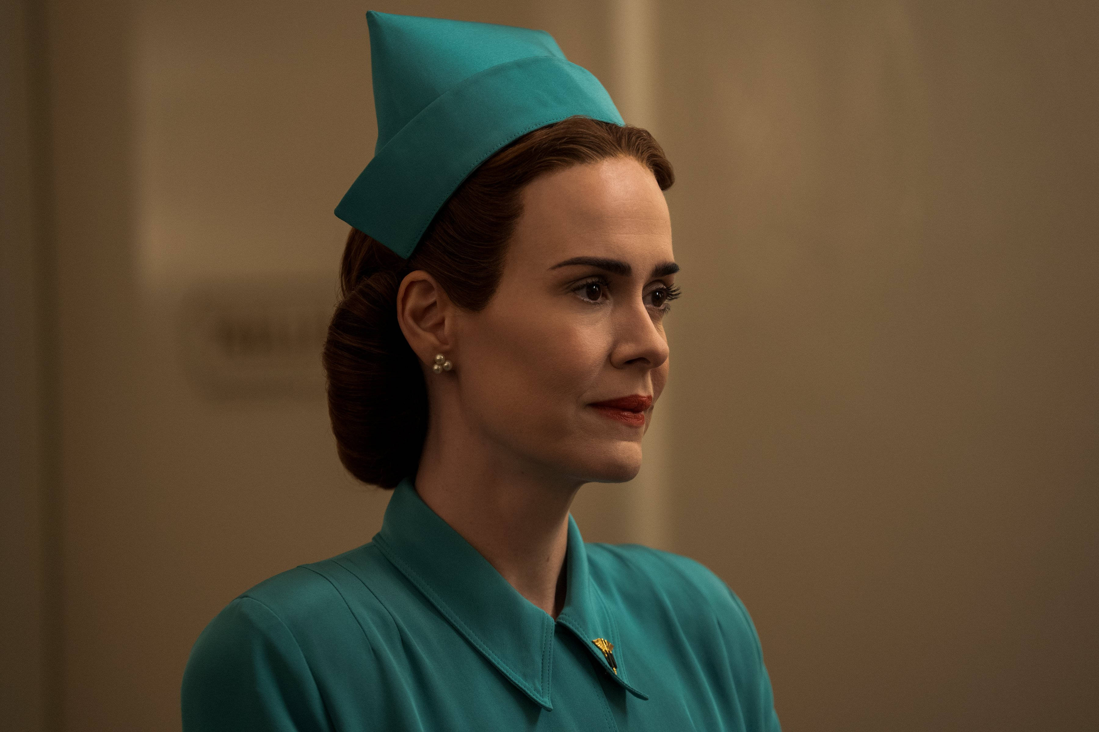 迷人 Nurse Ratched 壁紙 — 一位身穿藍綠色護士制服和相配帽子的女性，在柔和光線的室內環境中若有所思地凝視著旁邊。