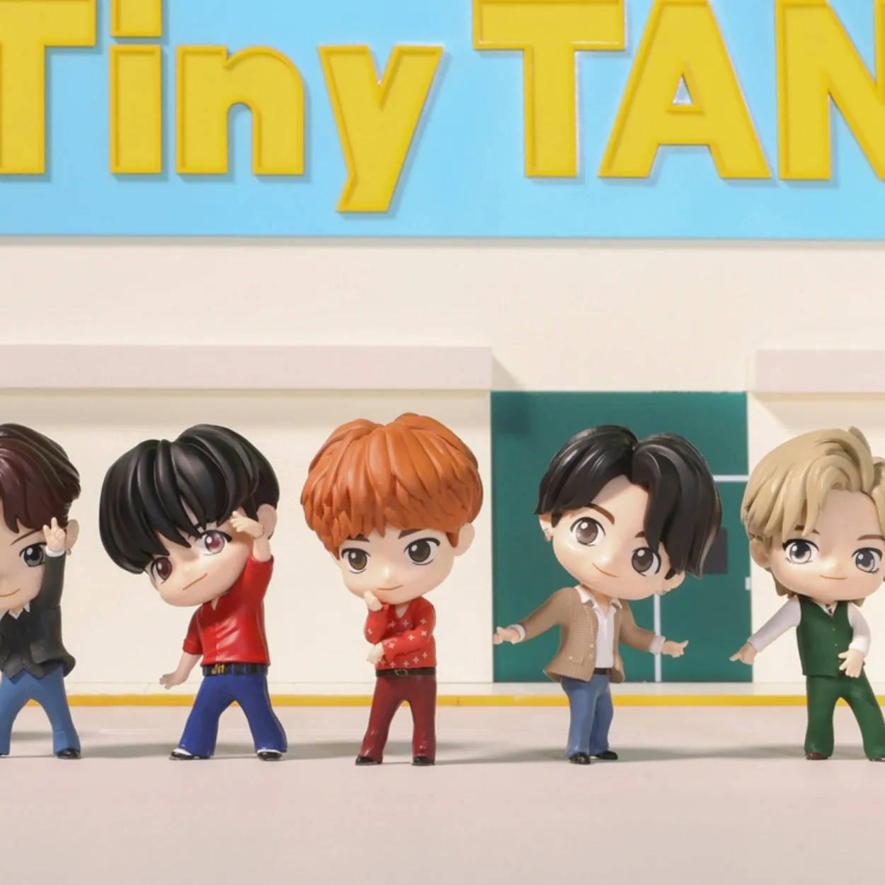 迷人 Tiny Tan BTS 玩偶動態演出 壁紙 — 五個Q版BTS公仔喺一個亮藍色嘅'Tiny TAN'招牌前面開心擺甫士，招牌上面有黃色字母。