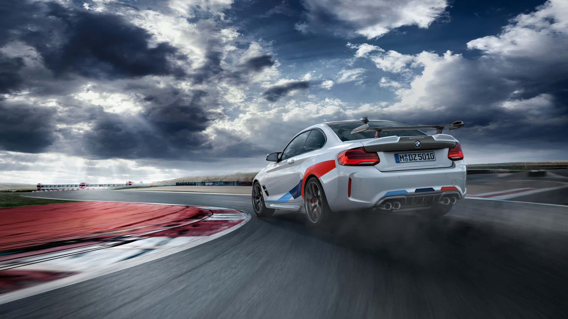 迷人1080p M系列背景 壁紙 — 一輛白色BMW M2賽車在戲劇性的多雲天空下於賽道彎角飄移。
