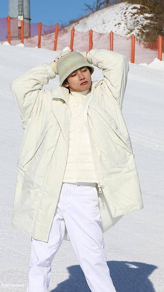 身穿奶油色冬季服裝的年輕人在雪地裡擺姿勢，旁邊有橙色圍欄。