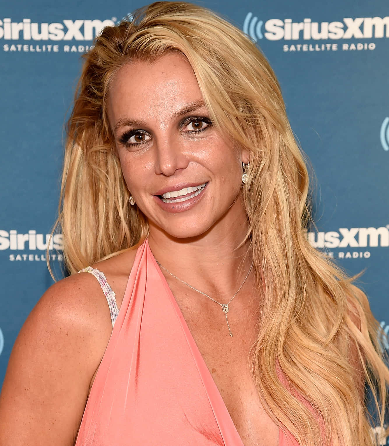 Britney Spears 在SiriusXM活動中穿著珊瑚色連衣裙微笑。