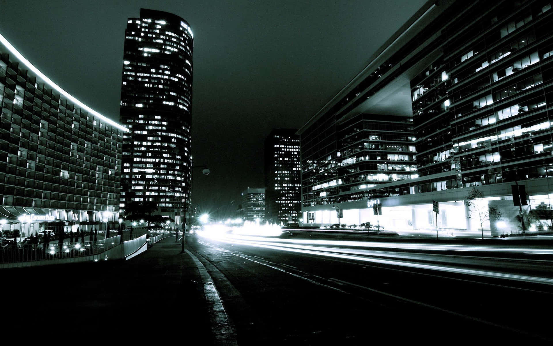 夜晚的城市街道，燈火通明的摩天大樓之間有移動車輛留下的光軌。
