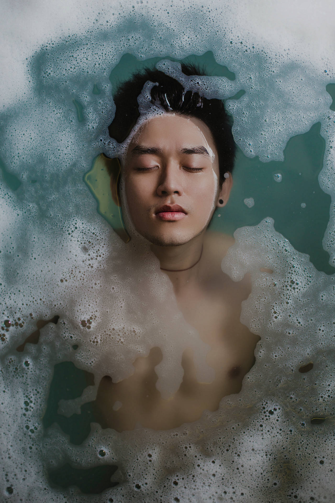 一個閉上眼睛的男子漂浮在藍綠色水的泡泡浴中。