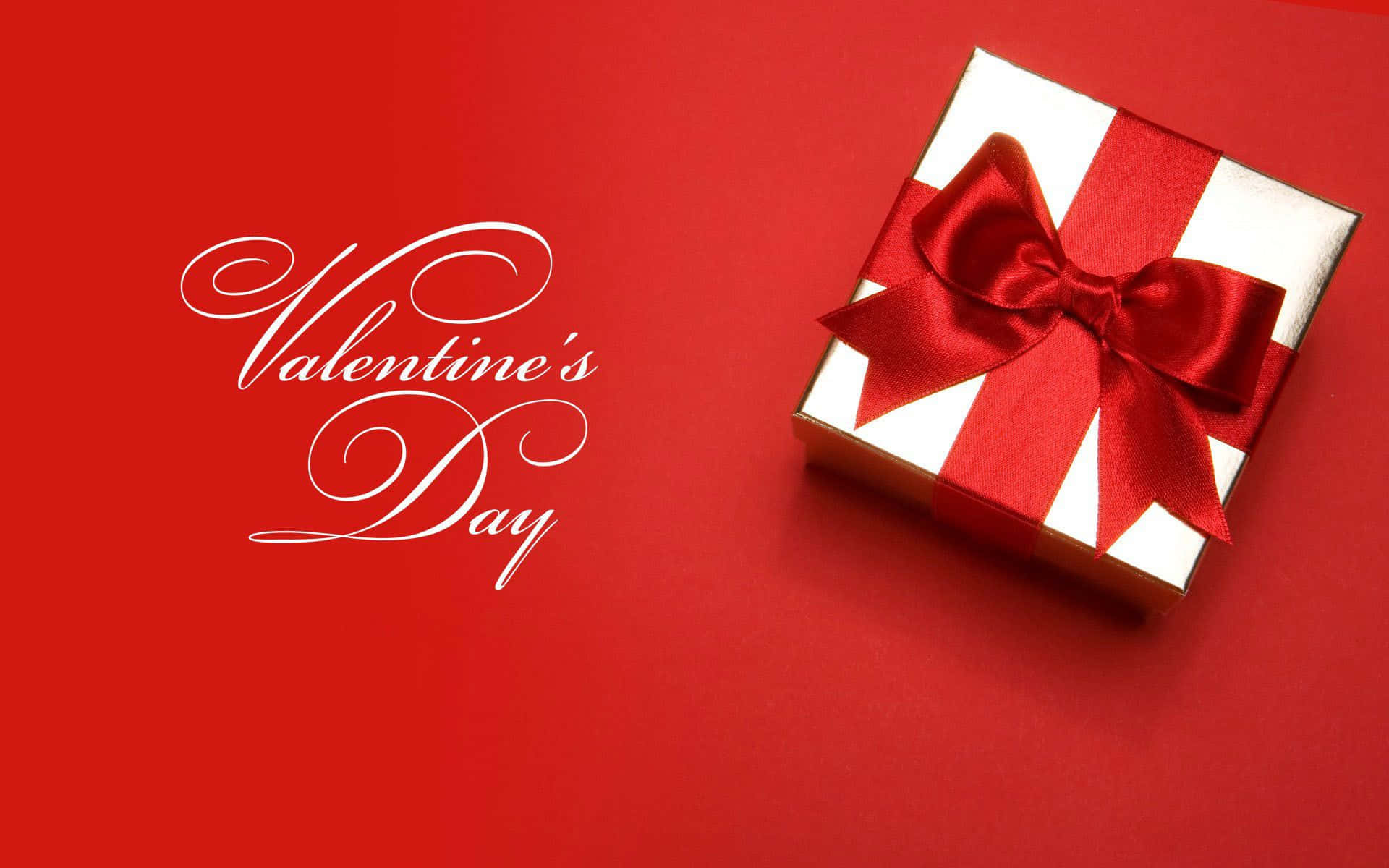 白色禮物盒配紅色蝴蝶結及Valentine's Day文字，紅色背景。