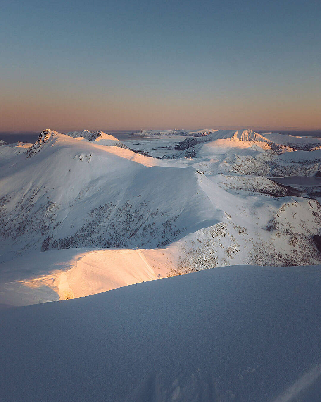 迷人天空高清壁紙 壁紙 — 夕陽將積雪的山峰沐浴在溫暖的金色光芒中，映襯著清澈的暮色天空。
