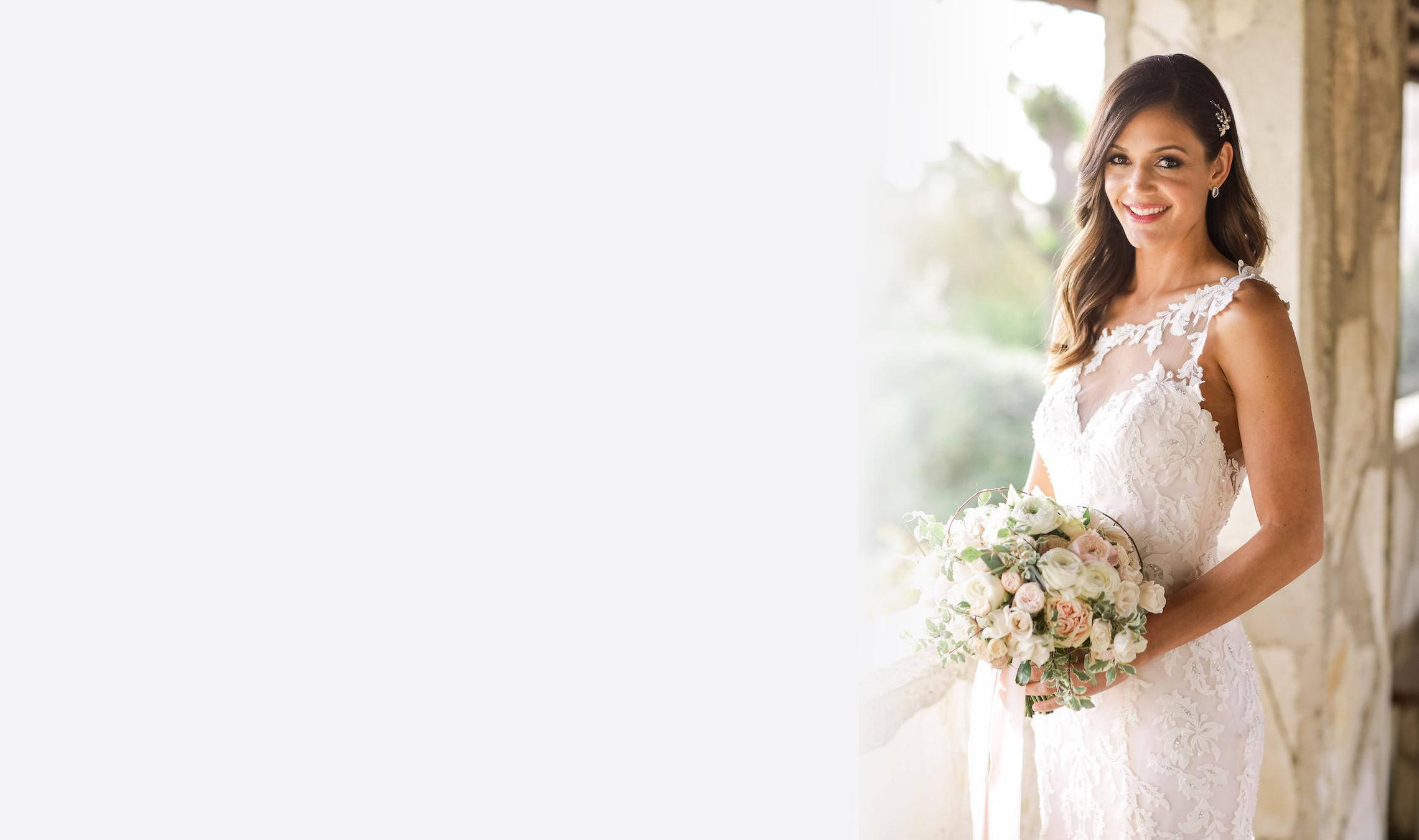 迷人婚禮美態 壁紙 — 一位身穿白色蕾絲婚紗的新娘在明亮的日光下微笑，手持柔和的粉彩花束。