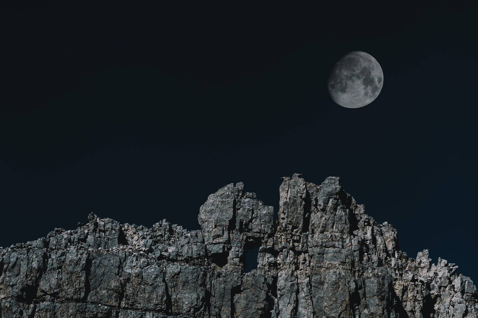 滿月在夜間從尖銳的岩石山峰上升起。