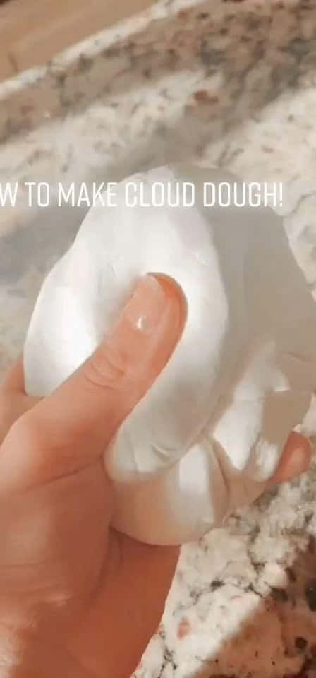 迷人星系史萊姆 壁紙 — 一隻手輕輕擠壓柔軟的白色雲朵麵團，放在有斑點的檯面上。
