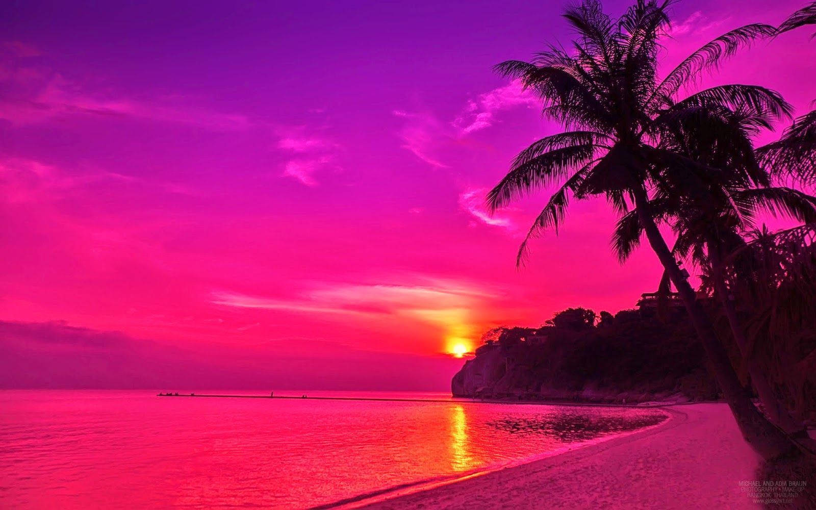迷人海灘夕陽風情 壁紙 — 超現實的粉紅和紫色日落，映照在寧靜的海灘上，棕櫚樹的剪影和平靜的水面反射著火熱的天空。