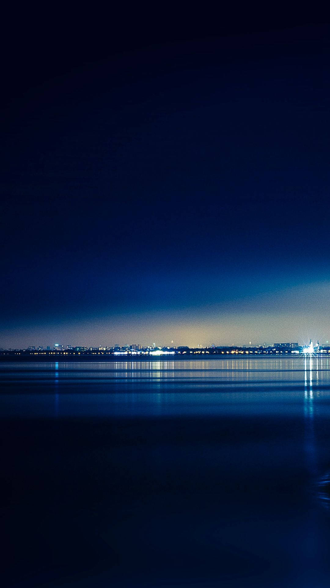 城市燈光倒映在平靜的水面上，背景是深藍色的夜空。