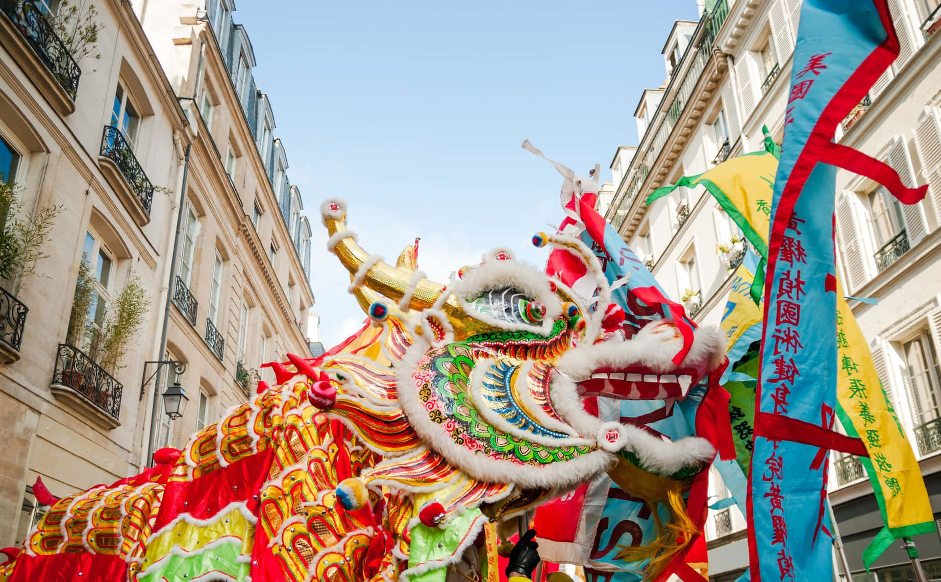 迷人的中國新年節慶 壁紙 — 一件色彩鮮豔、裝飾精緻的中國舞龍服裝，在晴朗的藍天下沿著狹窄的歐洲街道遊行。