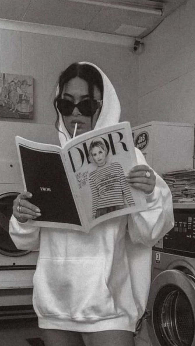 穿著連帽衫和太陽眼鏡的人在洗衣店裡拿著吸管閱讀Dior雜誌。