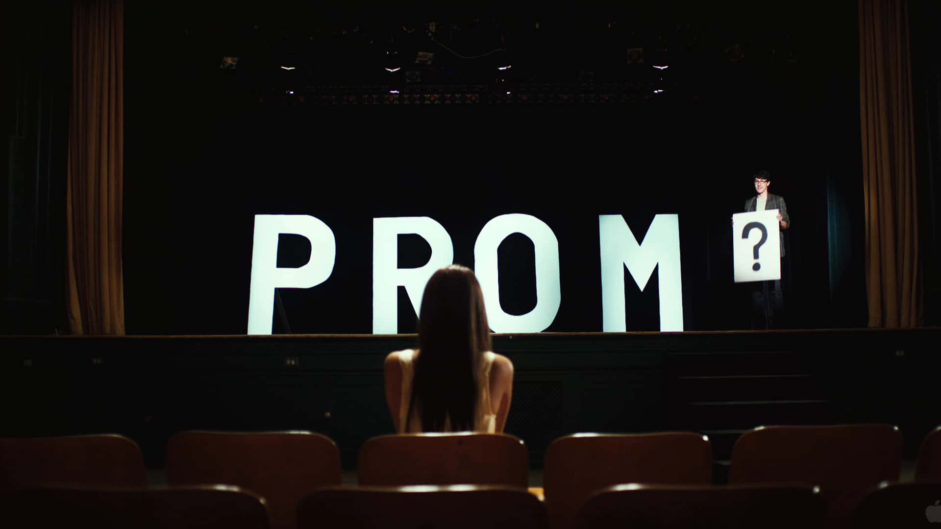 女孩看著帶有「PROM」和問號牌子的舞台。