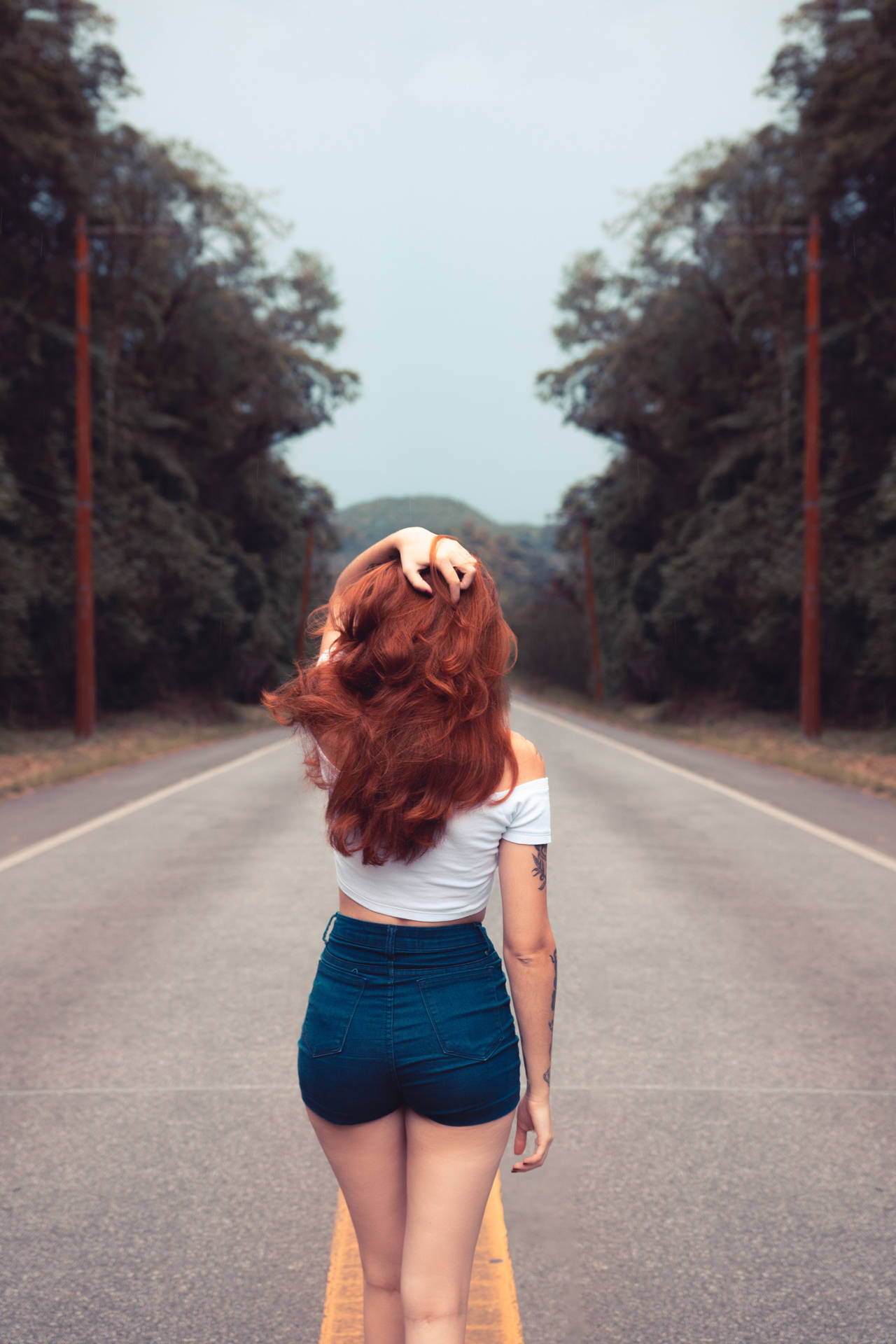 紅髮女子站在被樹木環繞的道路上