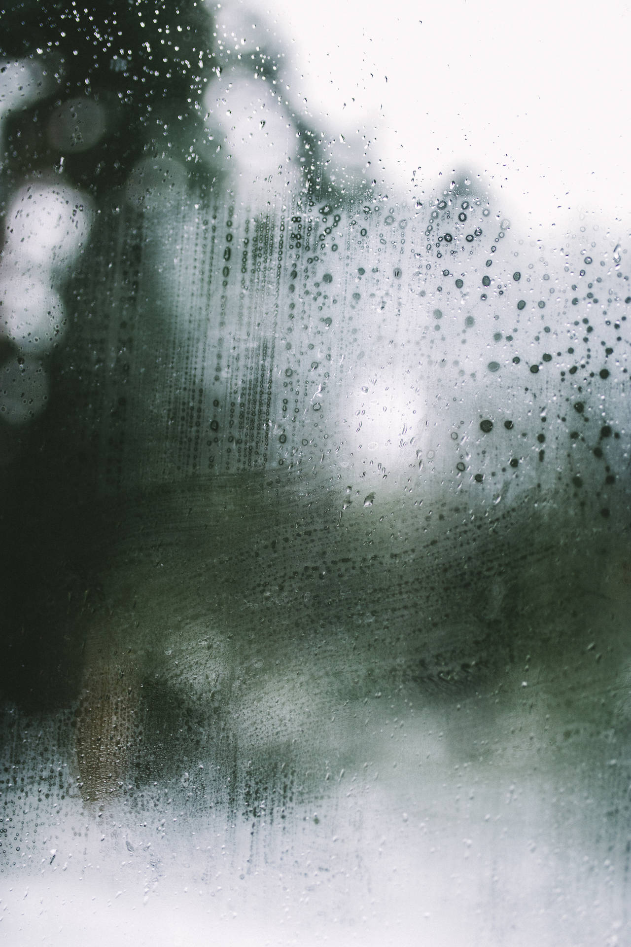 窗戶上的雨滴，背景有模糊的綠色樹木和柔和的白色光線