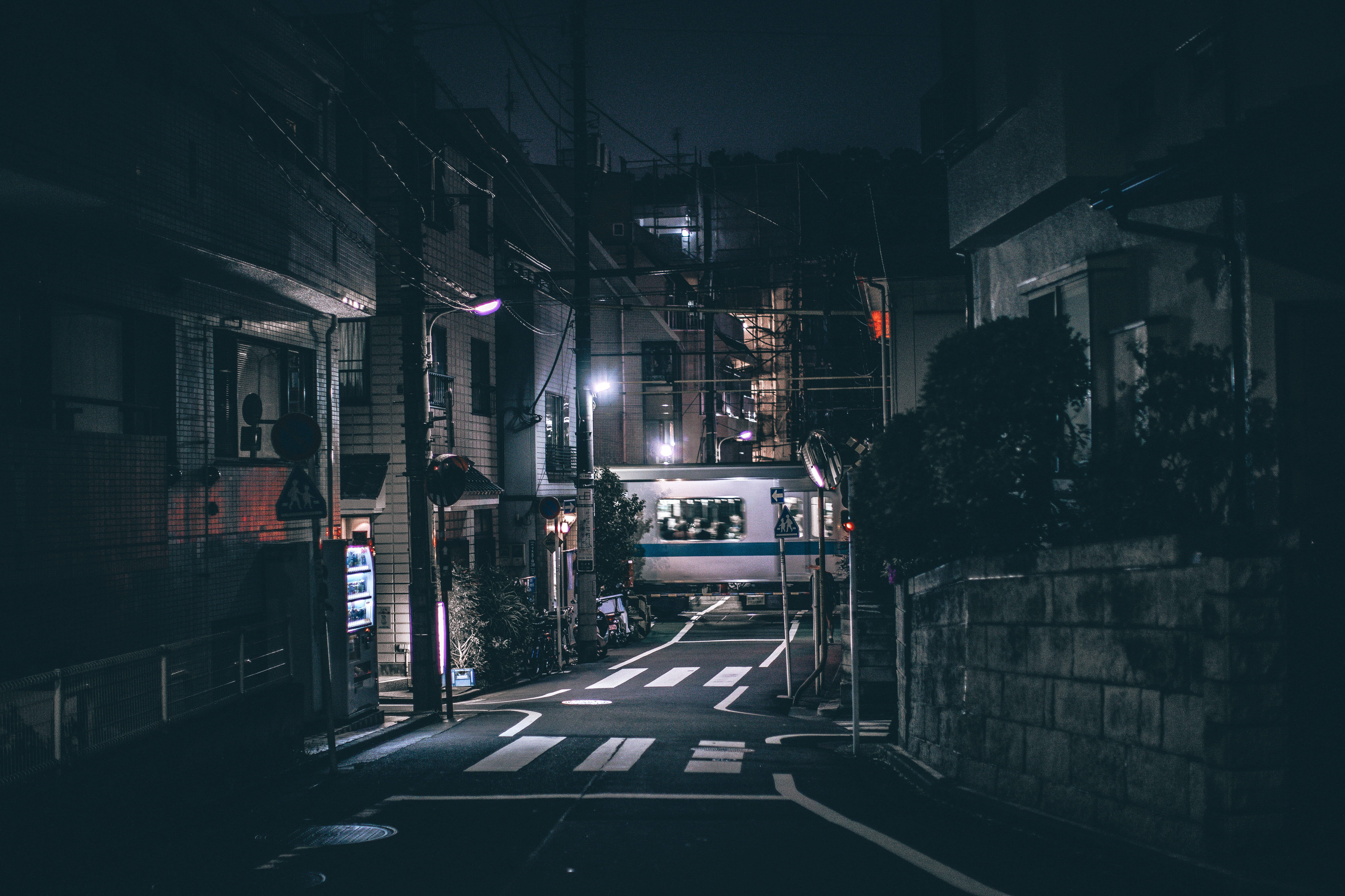 迷人空曠道路暗調4K 壁紙 — 夜晚一條狹窄的日本街道，被街燈和一列經過的火車照亮，在濕漉漉的路面上投下倒影。