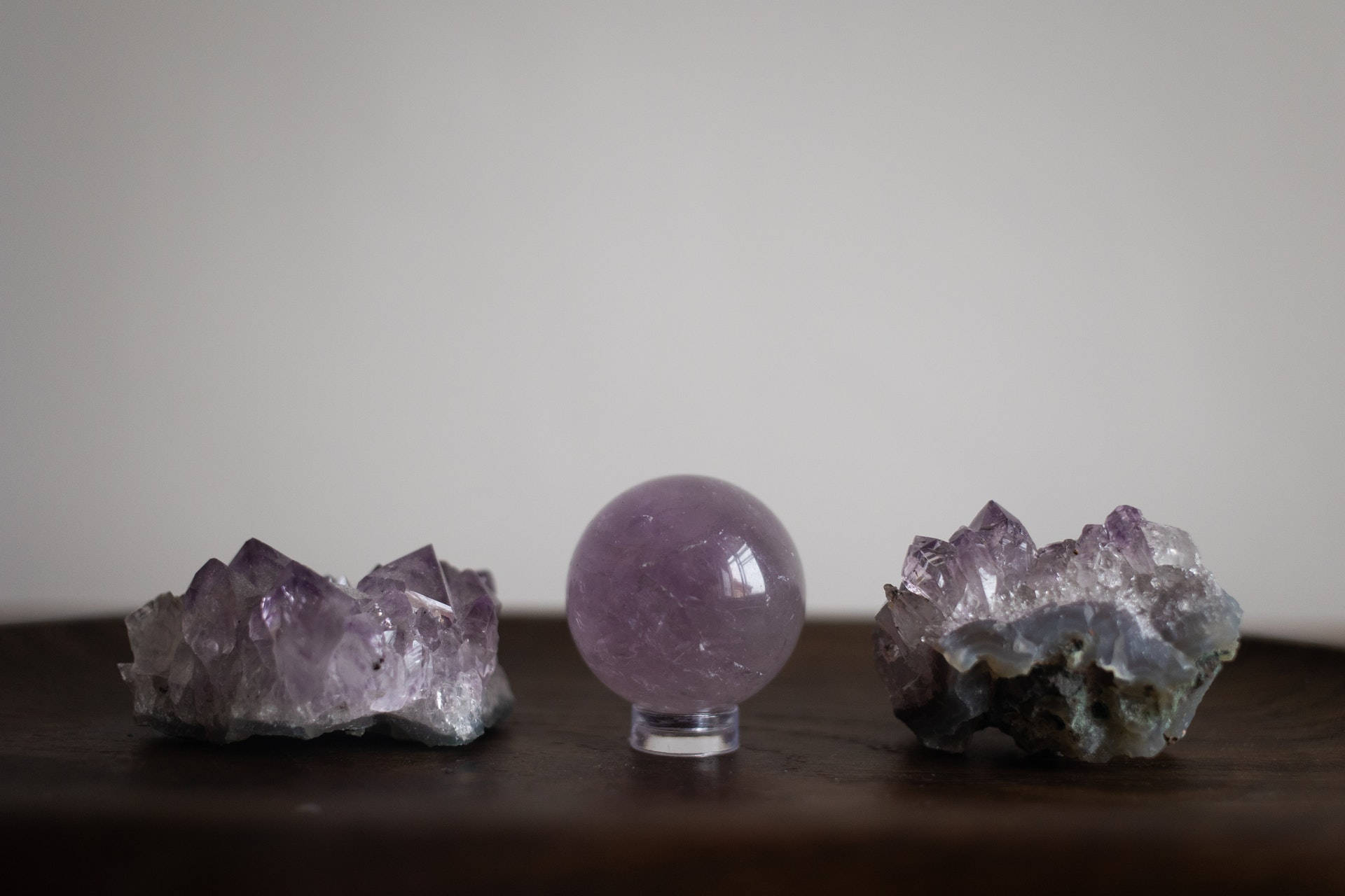 迷人紫水晶產品展示 壁紙 — 三塊紫水晶晶體和一個拋光球體放在深色木質表面上，背景是素牆。