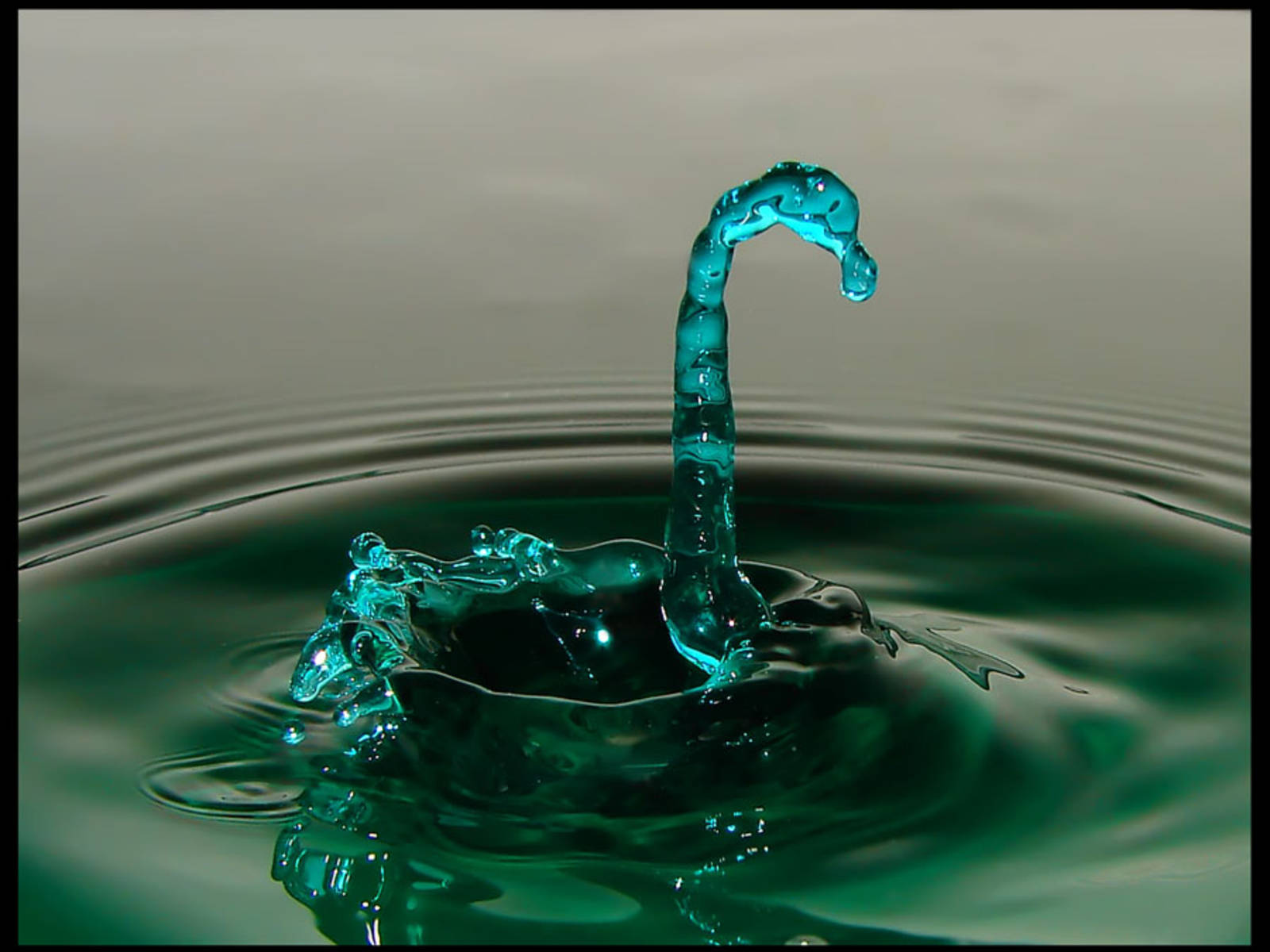 迷人翠綠水域 壁紙 — 一顆充滿活力的藍綠色水滴從漣漪池中向上拱起，形成短暫的雕塑般水花。