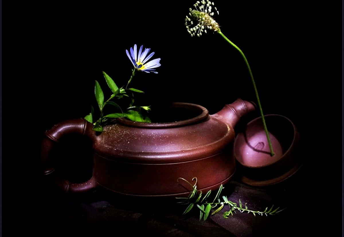 迷人薰衣草茶靜物藝術 壁紙 — 一個質樸的棕色茶壺，在純黑背景下，托著一朵精緻的藍色花朵和一根纖細的綠色莖。