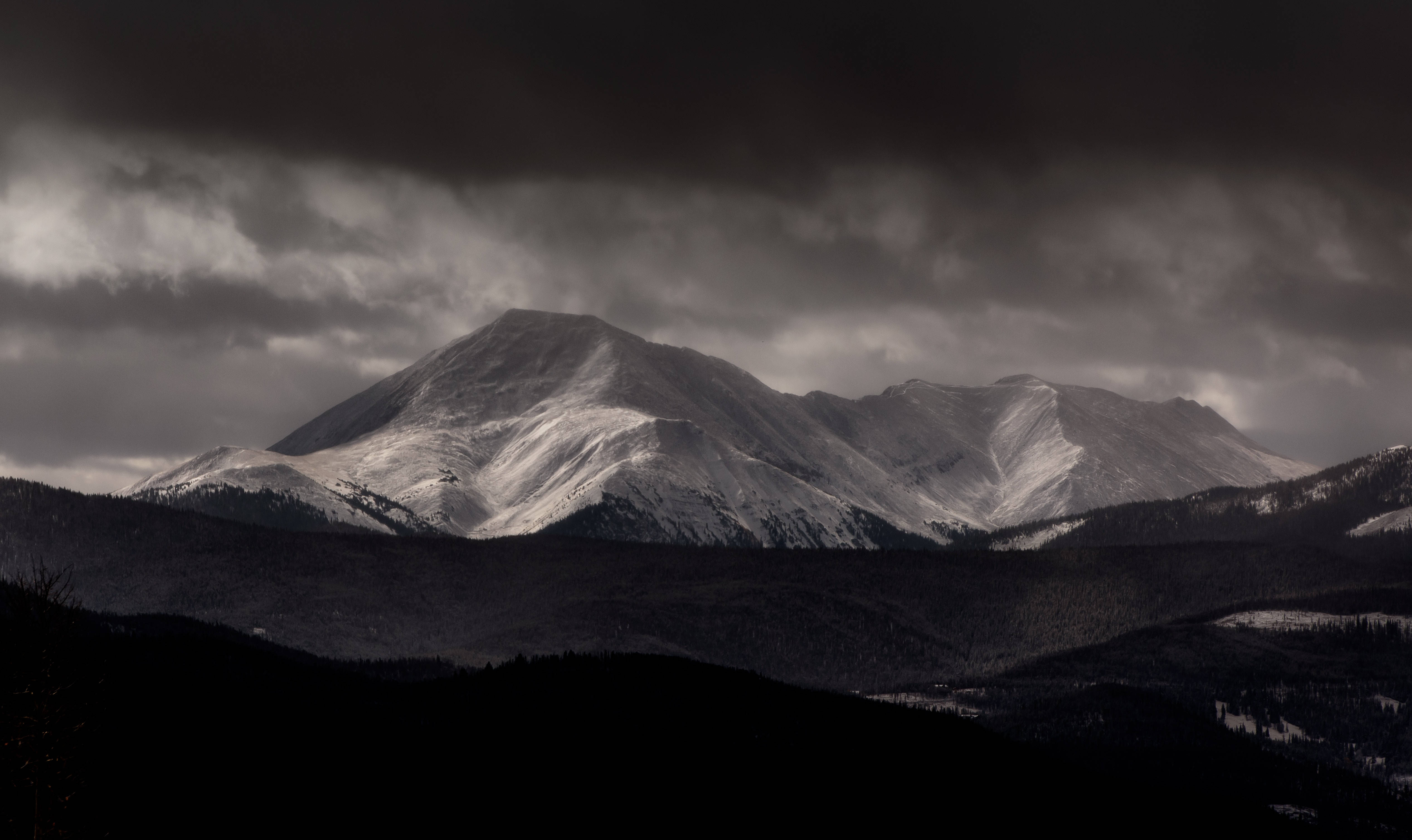 迷人雪山暗調4K 壁紙 — 一條戲劇性的山脈，白雪覆蓋的山峰在佈滿烏雲的沉重暴風雨天空下巍然聳立。